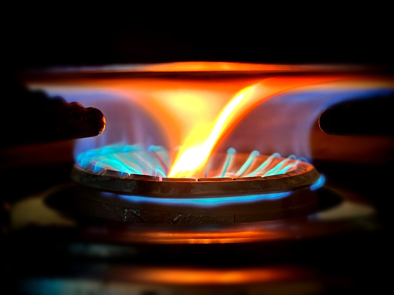 Services Close-up view of vibrant blue and orange flames on a gas stove burner.