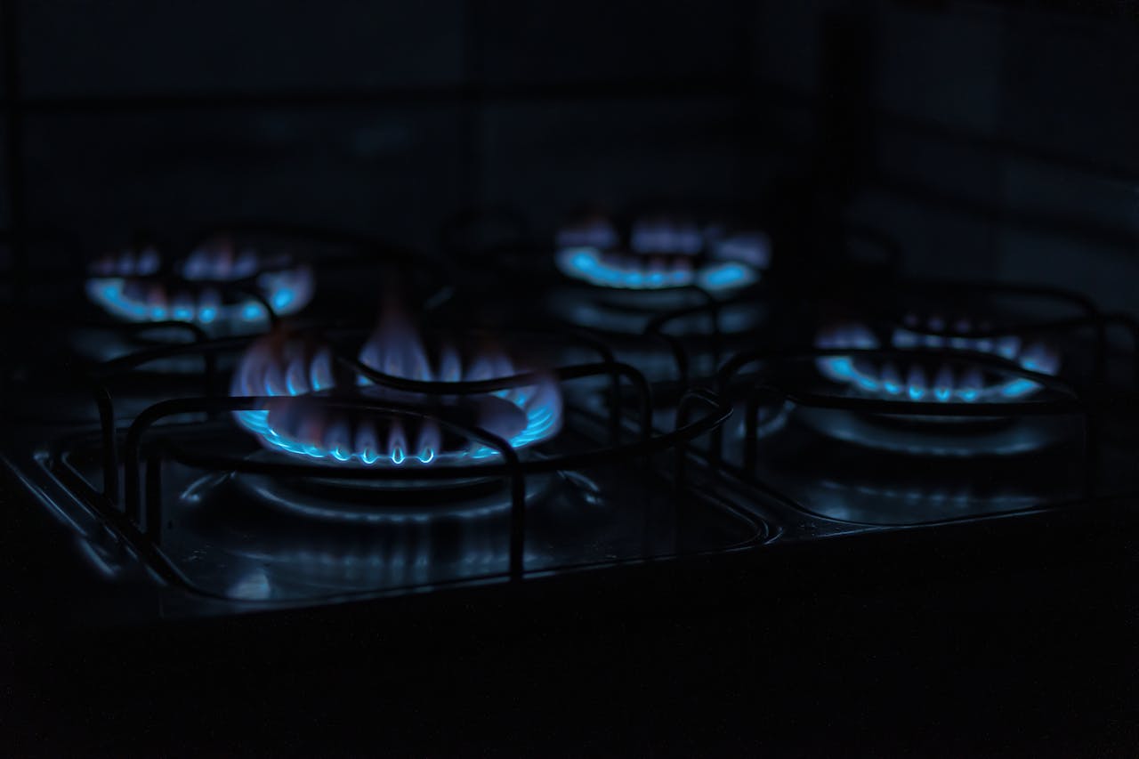 Home A dark, atmospheric image capturing the blue flames of gas stove burners indoors.