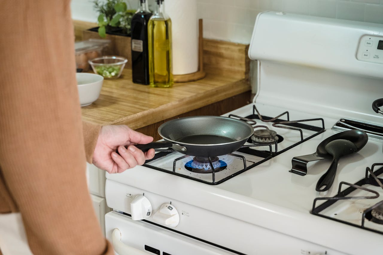 Home Close-up of a frying pan held over a gas burner on a stove, with kitchen essentials nearby.